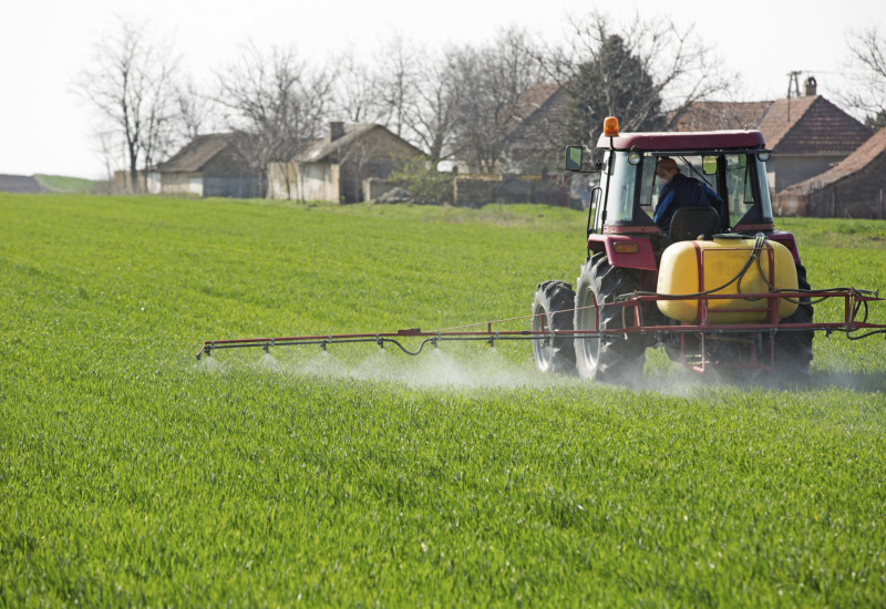 Ein Traktor fährt über ein grünes Feld und versprüht Pflanzenschutzmittel.